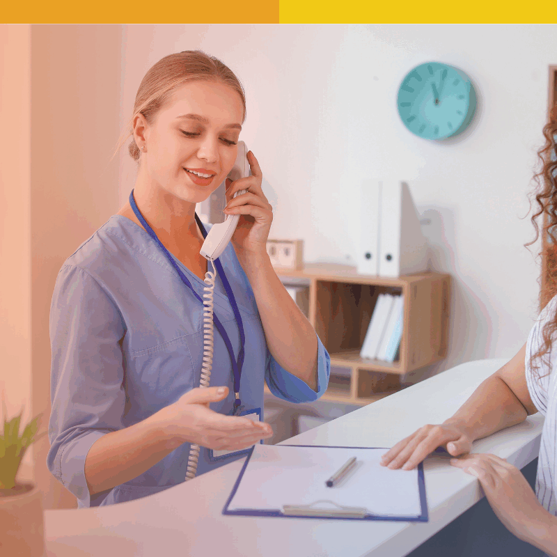 Receptionist at a vision center speaking on the phone while assisting a patient at the front desk.