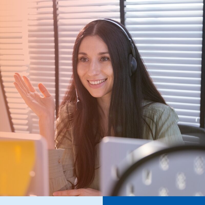 woman in corporate attire wearing a headset while using a laptop in office