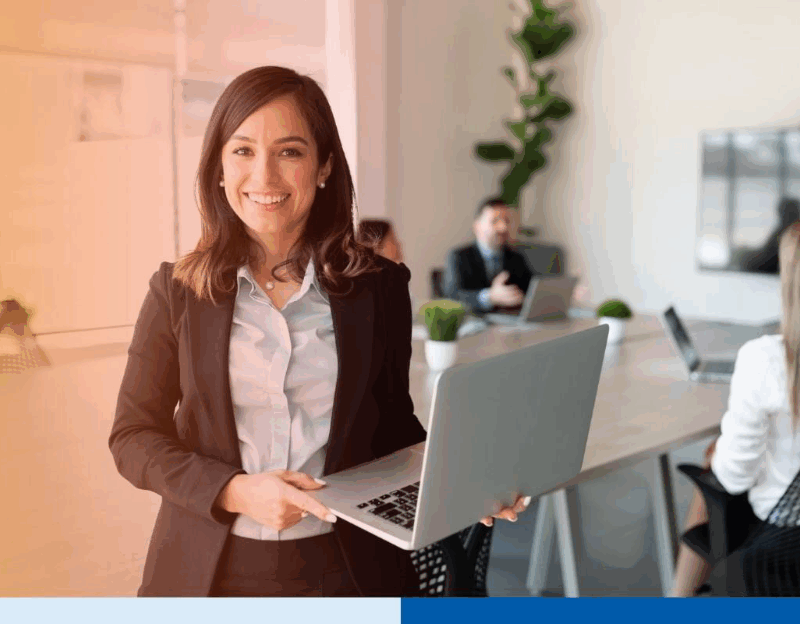 Portrait of smiling female entrepreneur holding a laptop with team in background at office conference room 