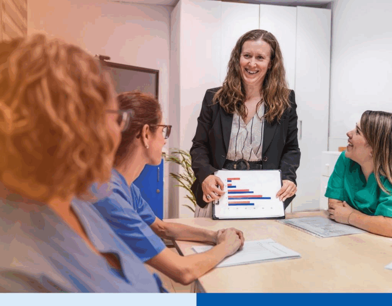 Nurses and a manager discussing data in a nursing home setting, focusing on teamwork and healthcare planning. A tablet displays relevant statistics