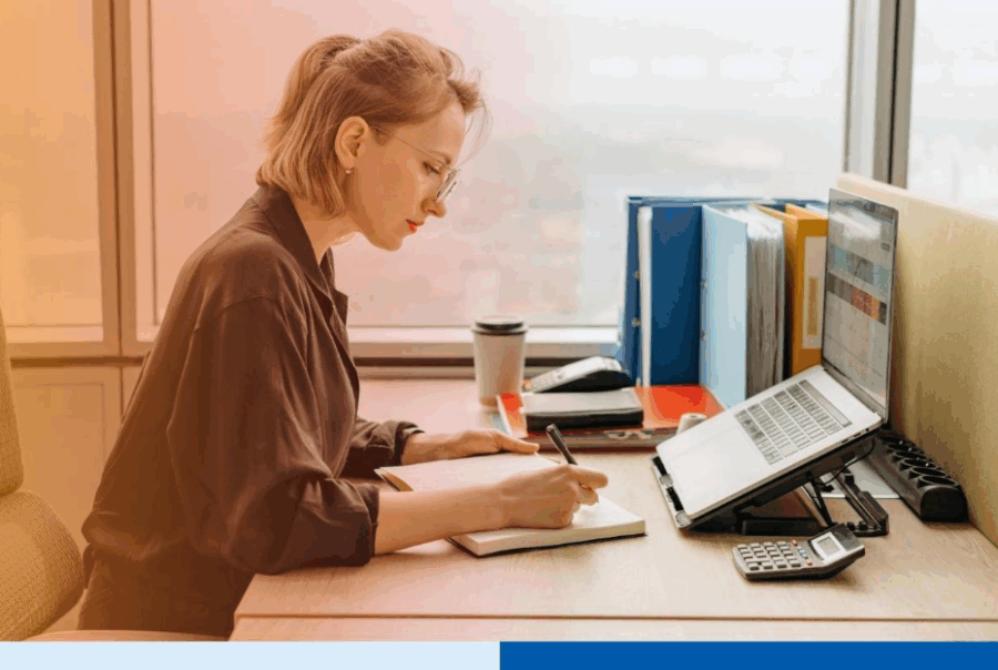 Professional woman working at her desk with a laptop and notebook in a modern office.Â
