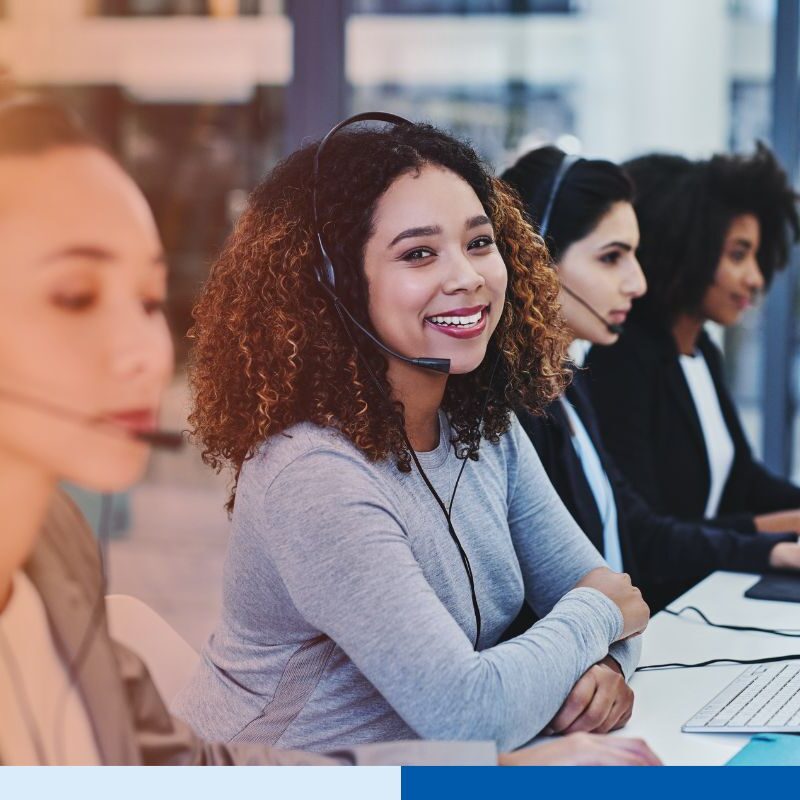 Smiling customer service representative wearing a headset while working with her team in a modern call center.