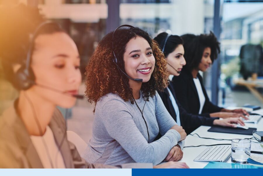 Smiling customer service representative wearing a headset while working with her team in a modern call center.