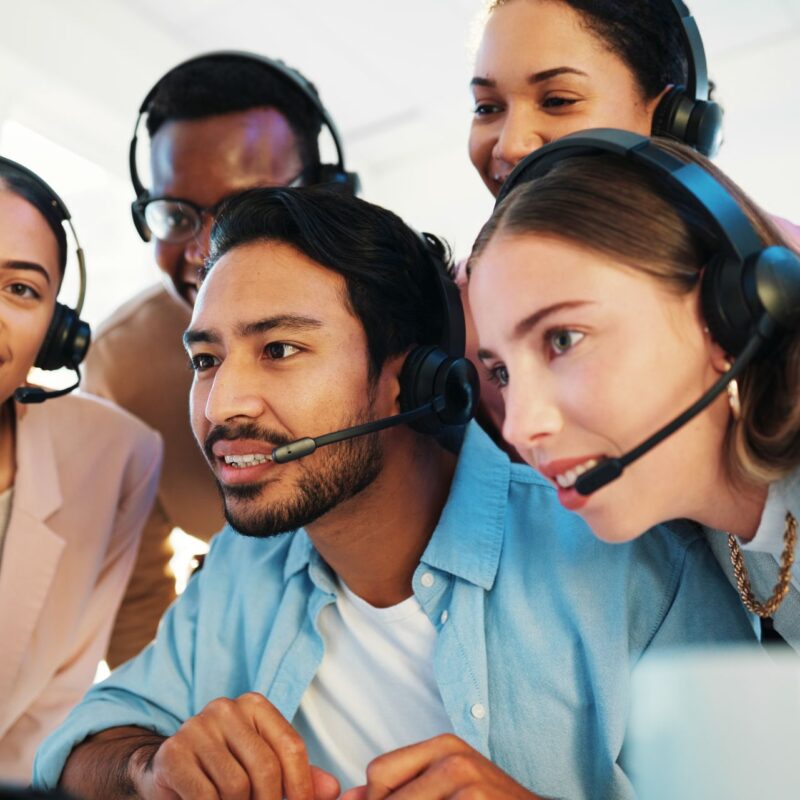 customer support team wearing headsets gathered around a computer, collaborating to resolve a client issue in a modern call center
